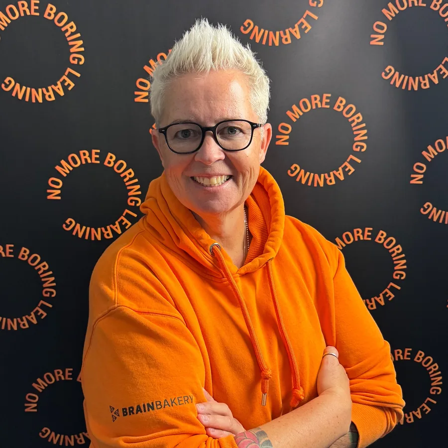 Jeanne Bakker in een oranje Brain Bakery-hoodie voor een wand met No More Boring Learning